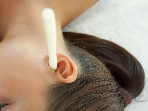 A close-up of an ear candle positioned at a person's ear.