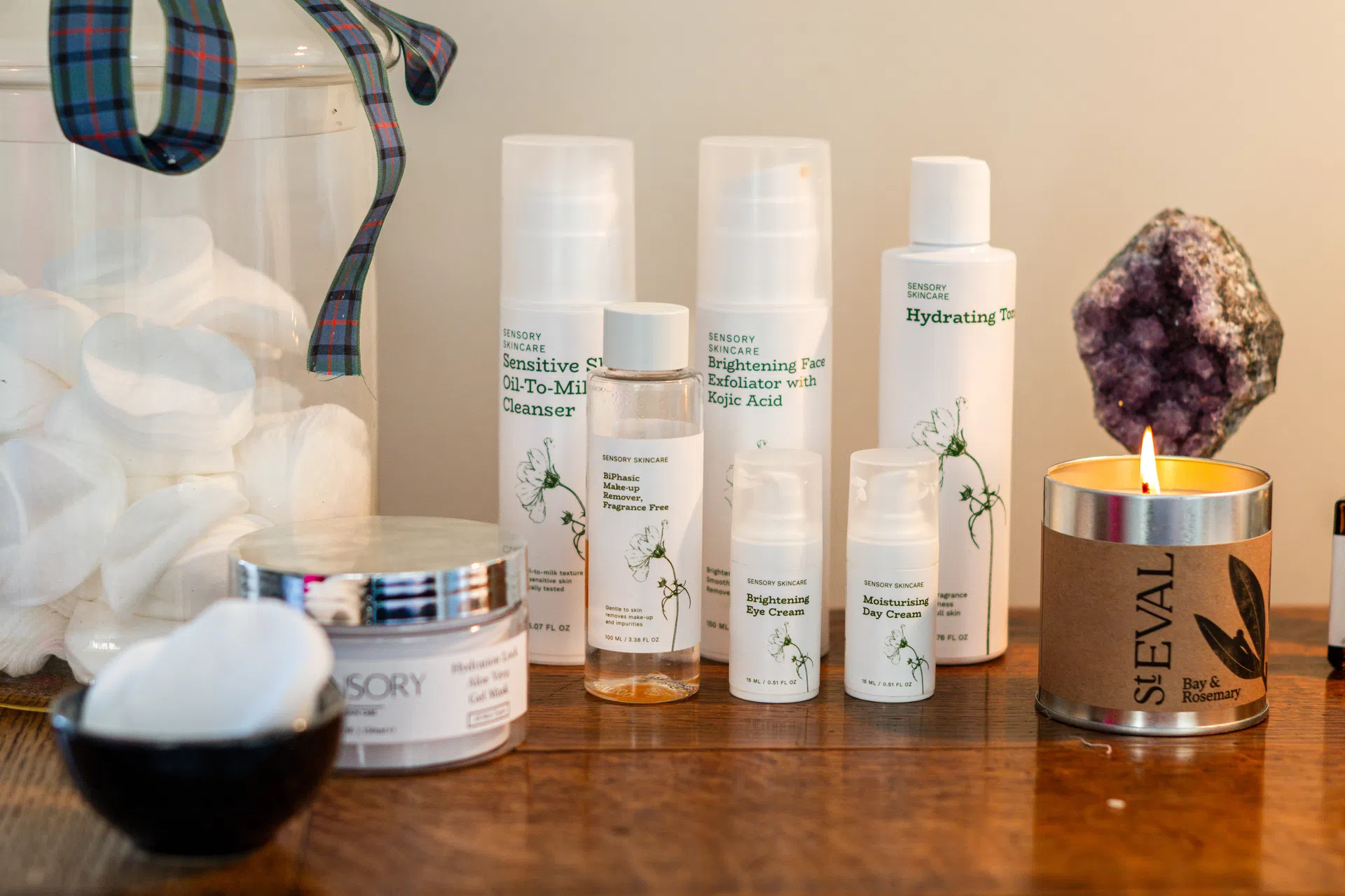 Facial skincare products, cleansing pads and a candle arranged for a treatment.