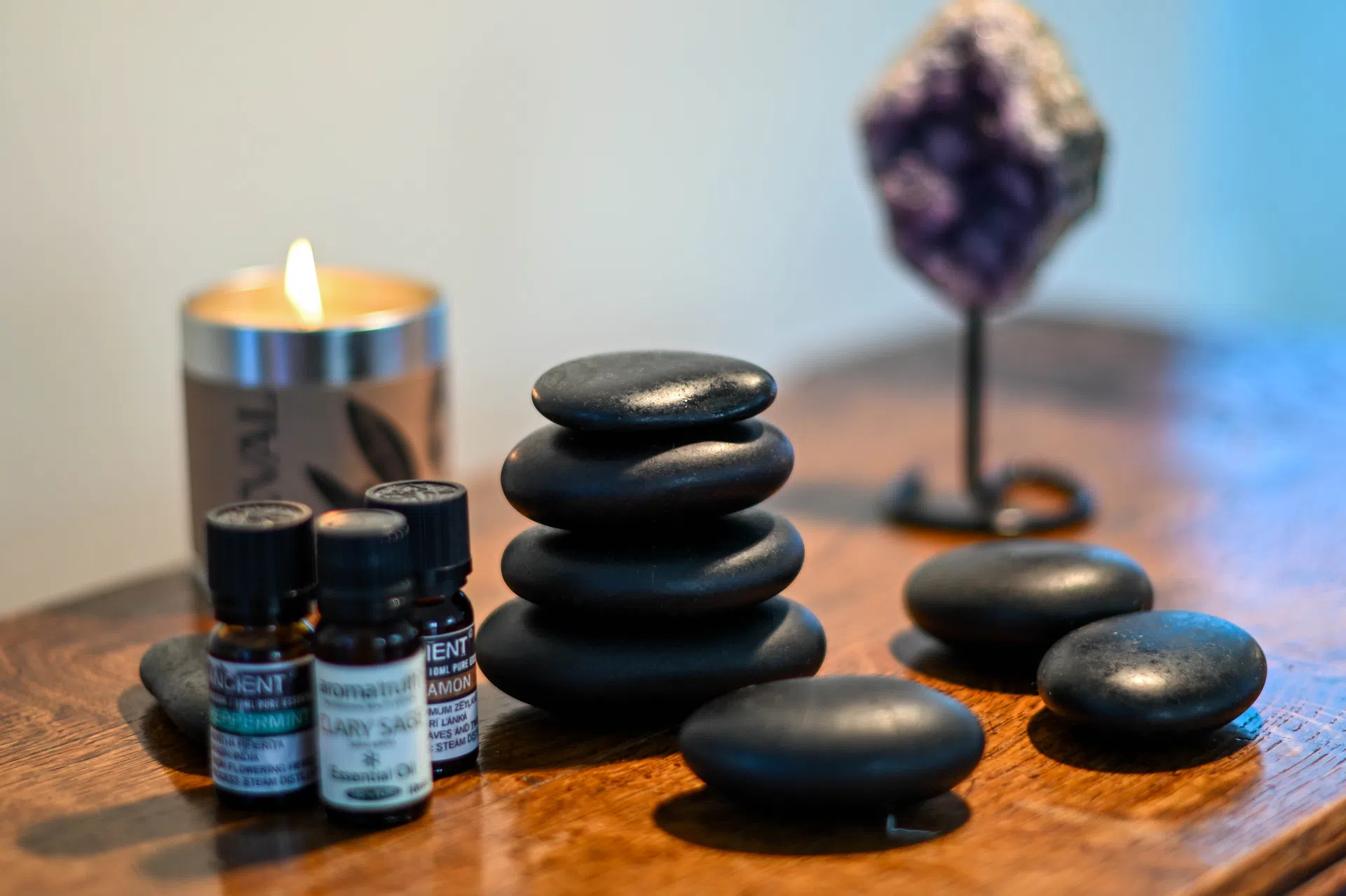 Smooth black massage stones, essential oil bottles and a lit candle.