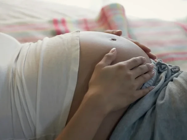 A pregnant person resting with their hands on their bump.